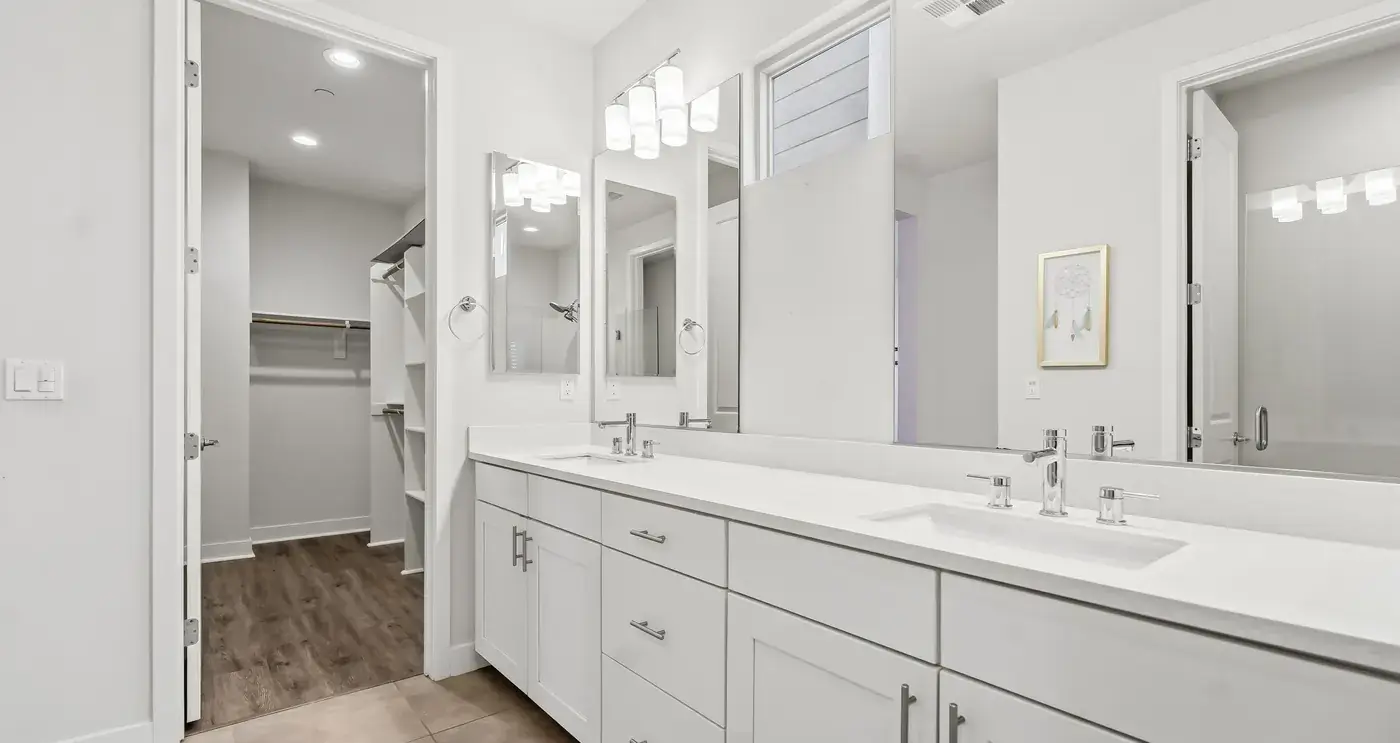 The owner’s bath: a long double vanity under a wide mirror, the walk-in closet beyond