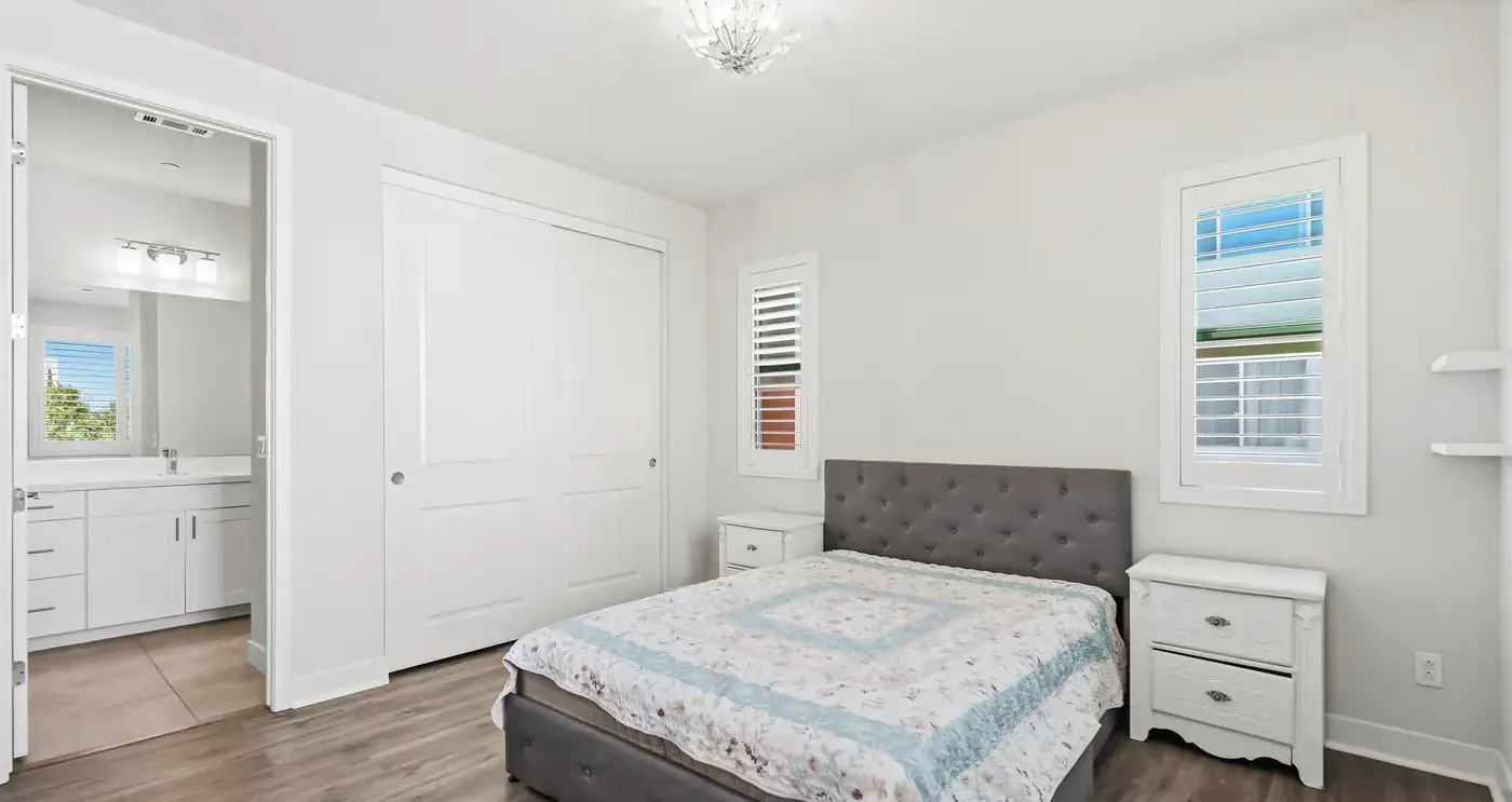 Bedroom 2: a bed with a white cover beside a window with plantation shutters
