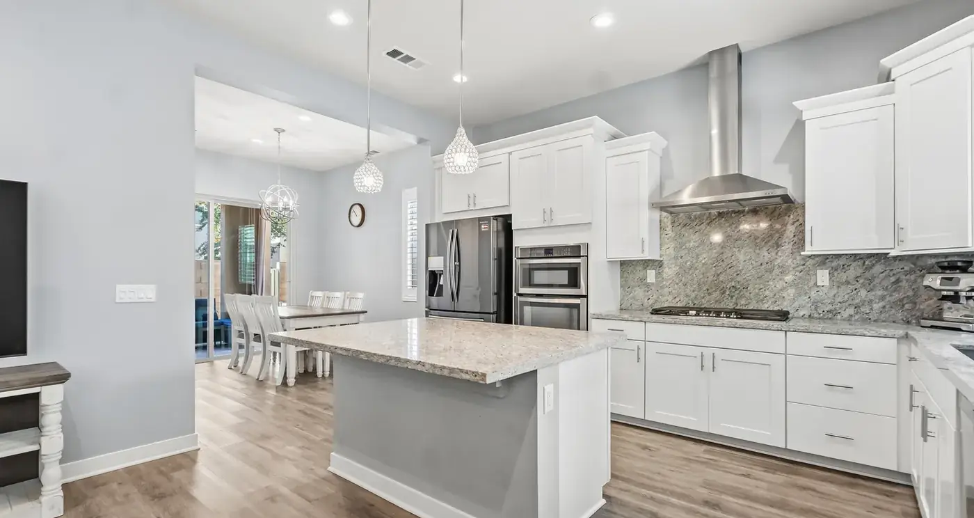 The kitchen: a granite island under pendant lights, white shaker cabinets, stainless appliances