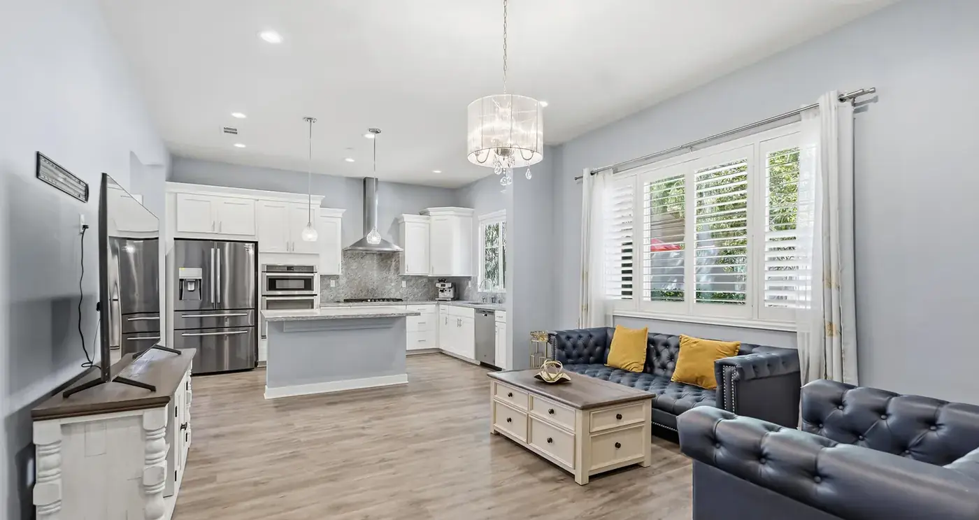 The gathering room: the dark leather sectional with yellow cushions under the windows, the kitchen and island beyond