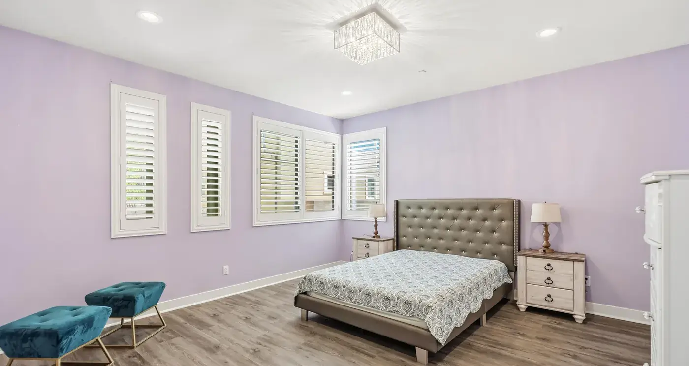 The owner’s suite: an upholstered bed, lavender walls and three windows with plantation shutters